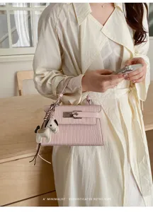 Close-up detail shot of stylish pink crocodile pattern handbag featuring cute horse charm.