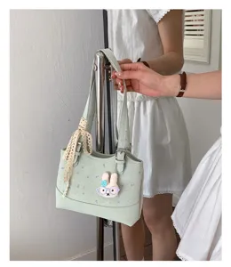 Close-up detail of light green shoulder bag featuring cute bunny pendant and lace ribbon.