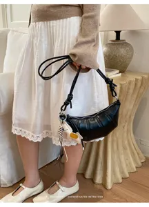 Detail shot of a black crescent croissant shoulder bag with knotted strap and chic charm accessory.