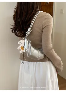 Detail view of silver metallic croissant shoulder bag with cute charm and knotted strap.