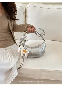 Silver metallic croissant dumpling bag with knotted handle and cute horse charm for women.