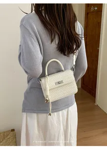 Vista detallada del elegante bolso cruzado tejido en color blanco con un broche metálico.