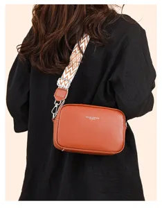 Brown leather crossbody bag detail featuring a stylish wide geometric strap and compact shape.