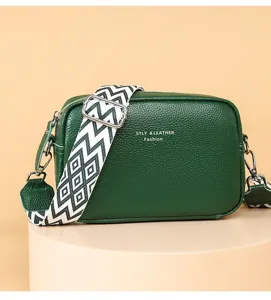 Detailed close-up view of the dark green leather crossbody bag with stylish wide patterned strap.