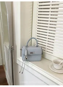 Elegante bolso de mano minimalista de cuero tejido azul claro con asa y cierre metálico.