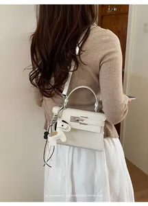 Detail view of white crocodile pattern shoulder bag featuring elegant top handle and cute horse charm.