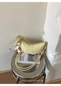 Detail view of minimalist yellow croissant crossbody bag with cute charm on metal stool.