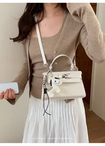 Detail view of white crocodile texture Kelly shoulder bag featuring cute horse charm and metal lock.