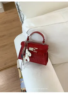 Detail view of a luxurious red crocodile textured Kelly handbag featuring an elegant horse charm.