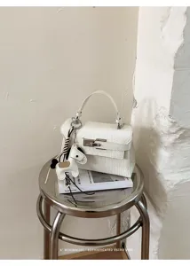 White crocodile texture leather Kelly handbag with chic horse charm and metal lock closure.