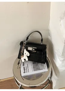 Detailed view of a black crocodile pattern handbag on a metallic stool with a horse charm.