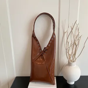 Detail view of brown glossy oil wax leather shoulder bag featuring metal grommets and strap.
