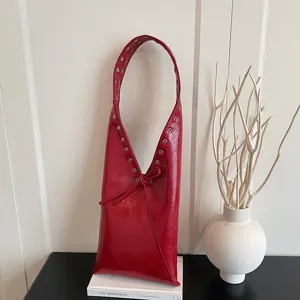 Red oil wax leather underarm bag detail, featuring metal rivet grommets and elegant strap decor.