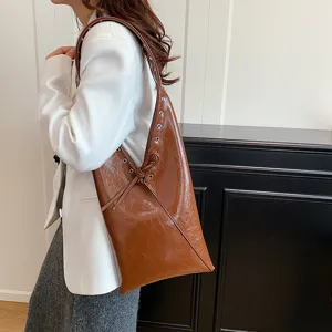 Detailed view of brown glossy leather shoulder hobo bag with metal grommets and strap design.