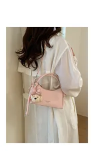 Detail shot of a stylish pink shoulder handbag featuring a cute plush puppy and bow charm.