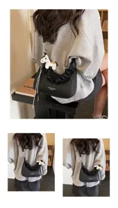 Black ruched shoulder bag detail view, featuring stylish leather texture and cute horse charm.