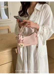 Detail view of a stylish pink women shoulder handbag with cute bear pendant and clean design.