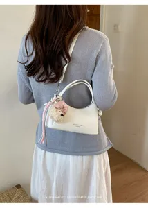 Detail view of stylish white shoulder handbag featuring a cute plush bear charm and bow.