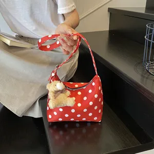 Detailed shot of red polka dot shoulder bag with cute bear pendant, stylish accessory closeup.