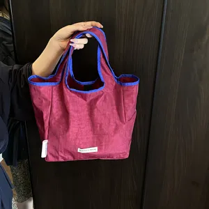 Detailed view of stylish folding reusable shopping tote bag in magenta with blue contrast trim.