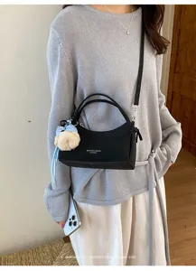 Detailed shot of stylish black leather shoulder bag with plush charm, minimalist style.