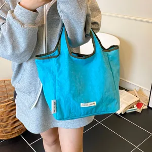Close detail of the vibrant blue canvas handbag showing neat brand label tags and sturdy straps.