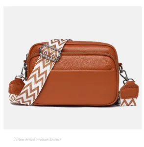 Close-up detail of the brown leather crossbody bag featuring a stylish geometric patterned wide strap.