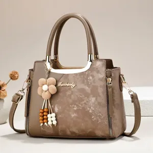Brown multi-layer handbag with metal top handle, floral charm and adjustable strap.