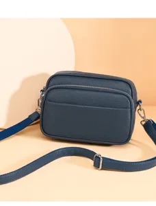 Close-up detail of dark blue leather crossbody bag, soft pebbled texture and metal zipper.