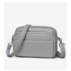Grey genuine leather crossbody bag detail, pebbled texture and silver zipper hardware.