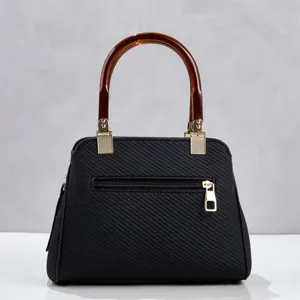 Détail rapproché du sac à main texturé noir avec poignée ambrée et quincaillerie dorée.