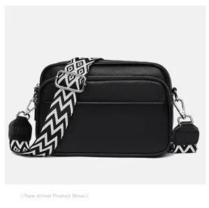Close-up detail of black leather crossbody bag with geometric wide strap and metal hardware.