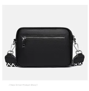 Black leather crossbody camera bag detail showing texture, metal zipper and patterned strap.