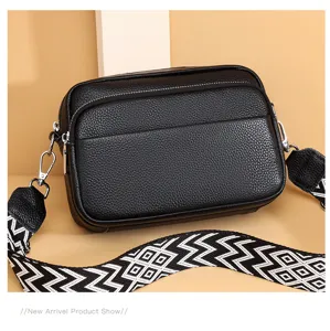 Black leather crossbody bag detail shot, featuring metal hardware and wide patterned strap.