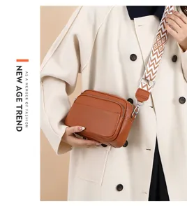 Detailed shot of textured brown leather crossbody bag with patterned wide strap and zipper.