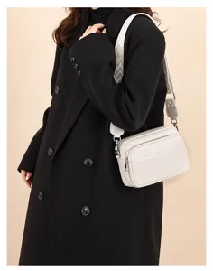 Close up of a stylish white leather crossbody bag with wide patterned strap detail.