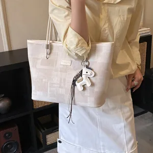 Vista dettagliata di una borsa tote beige in tela con ciondolo cavallo in pelle.