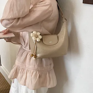 Dettaglio di borsa a sacco beige di tendenza con ciondolo floreale chic indossata a spalla.