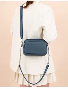 Detail view of a blue leather crossbody square bag with metal chain strap worn on model.