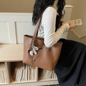 Detail view of a stylish brown leather tote bag with metal lock detail and cute charm pendant.