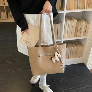 Detailed view of beige leather tote bag featuring metal turn lock and cute horse charm accessory.