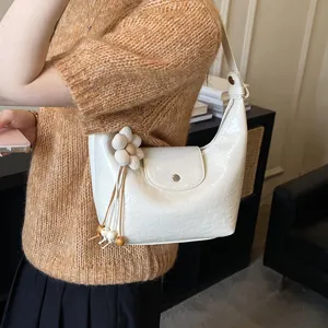 Primo piano di una borsa a spalla elegante in ecopelle bianca con ciondolo floreale.
