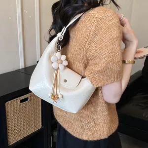 Dettaglio della borsa a spalla bianca con ciondolo a fiore e perline di legno decorative.