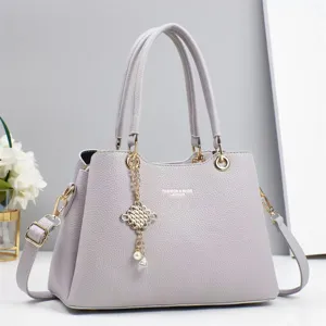 Detailed close-up of a stylish grey leather women's handbag with metal chain charm and handles.