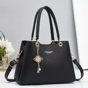 Close-up of black leather handbag detail, featuring gold hardware and elegant pearl charm.