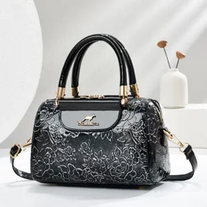 Close-up detail of black patent leather handbag with embossed flowers and gold clasp.