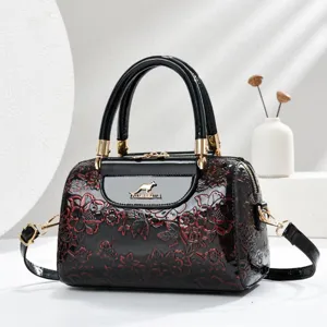Black patent leather handbag with red floral embossing, top handle and shoulder strap for women.