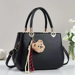 Close-up detail of a chic black handbag featuring gold hardware and a cute teddy bear plush charm.