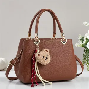 Brown leather handbag detail featuring cute plush bear pendant and elegant heart metal charm.