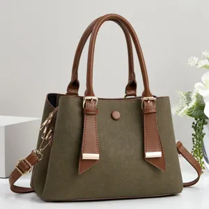 Dettaglio borsa in tela verde con manici in pelle marrone e finiture metalliche dorate.
